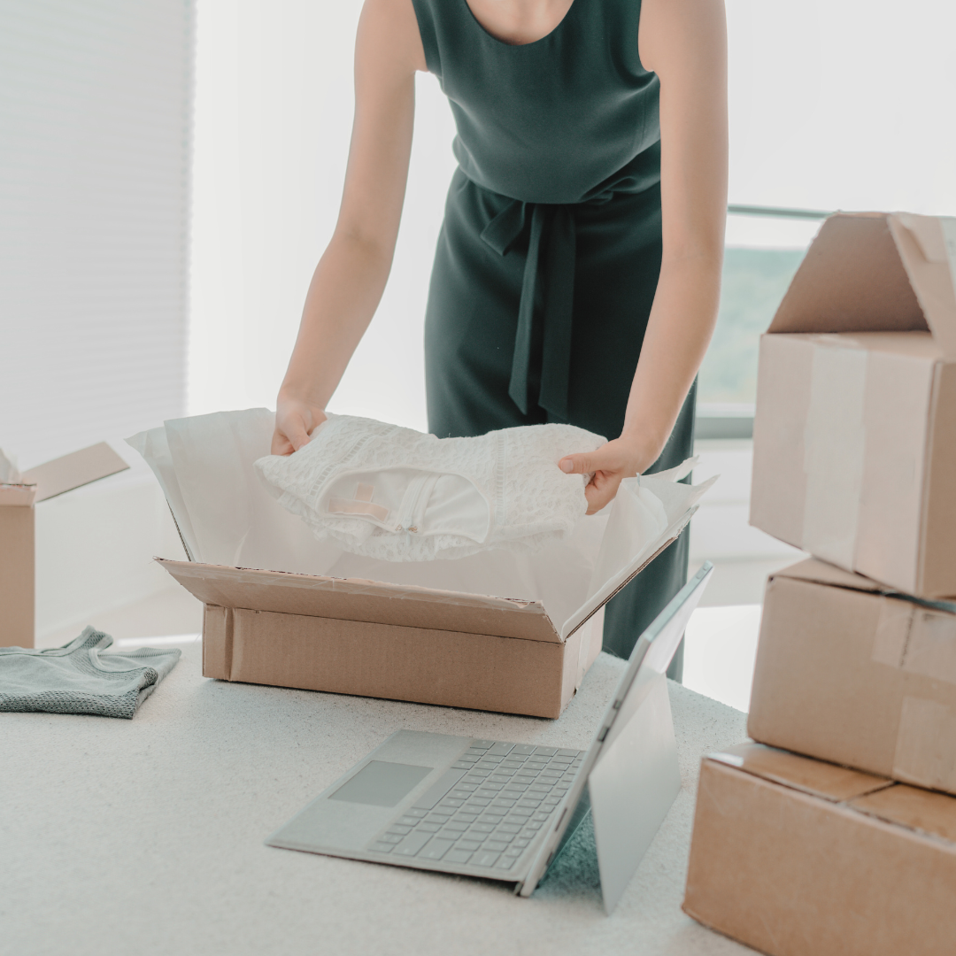 woman placing items into a box for shipping. several boxes are stacked to the side and ready to be shipped.