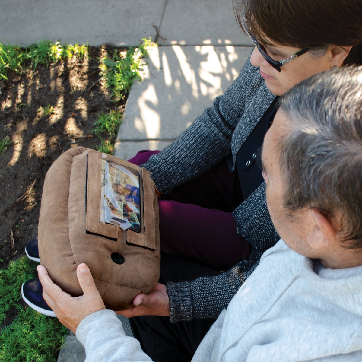 an older couple sitting outdoors holding a brown phone spud while watching a video on a phone