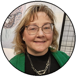 Person wearing glasses and a green jacket with a blurred background