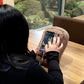 Woman uses brown potato pillow phone stand phone accessory for holding smartphone cell phone gaming scrolling watching videos comfortable phone use easing hand strain arthritis carpal tunnel