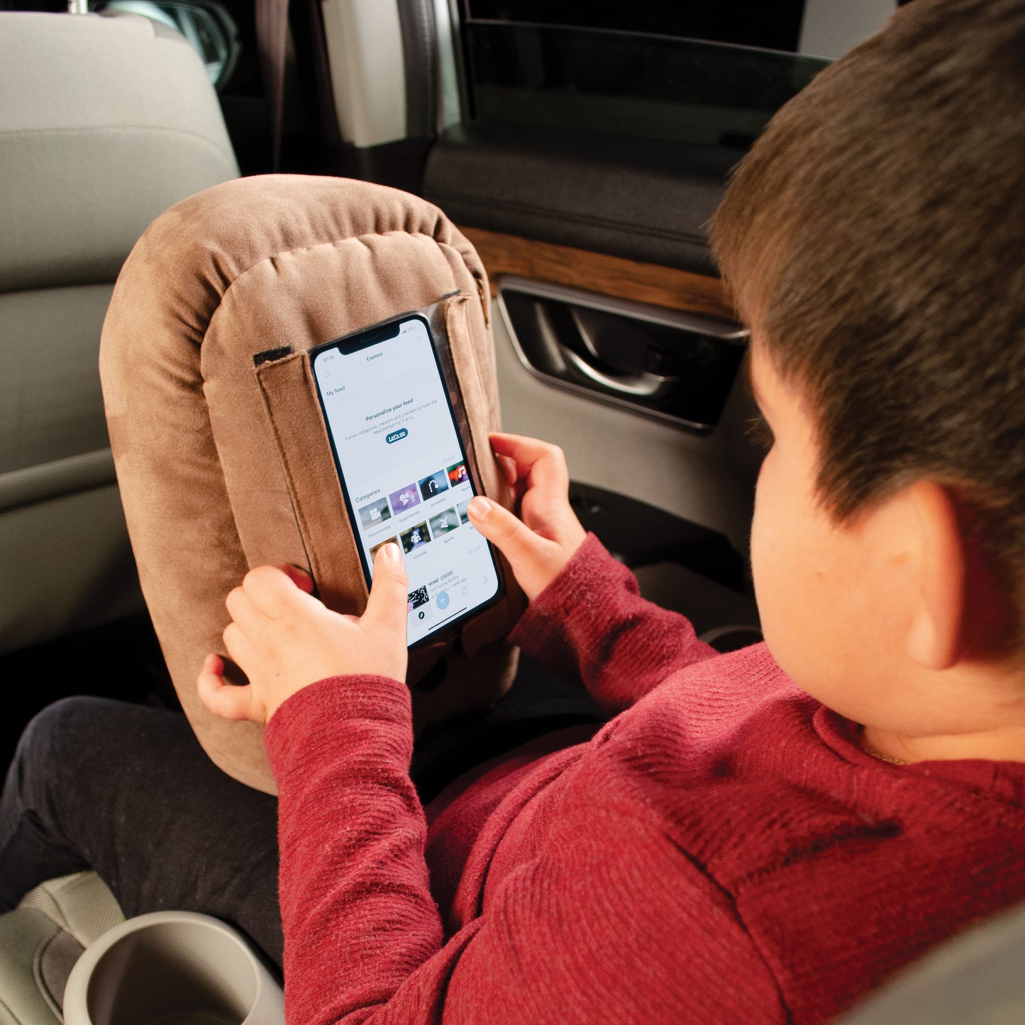 a child in the back seat of a car enjoying using his phone with a phone spud pillow